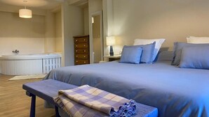 A bedroom with a bed, bedside tables, a bench, a lamp, and a bathroom with a bathtub. - apartamentos calm and nature (Cabezón de Liébana)