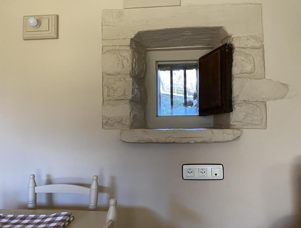 Una habitación con pared de piedra, una ventana pequeña, una silla y una mesa.