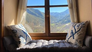 A window with a view of mountains, a cushioned bench with floral pillows, and a wooden frame. - apartamentos calm and nature (Cabezón de Liébana)