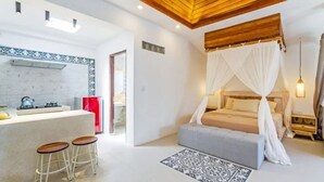 Quarto com cama de dossel, um pequeno espaço de estar com bancos, cozinha com fogão e um tapete estampado.