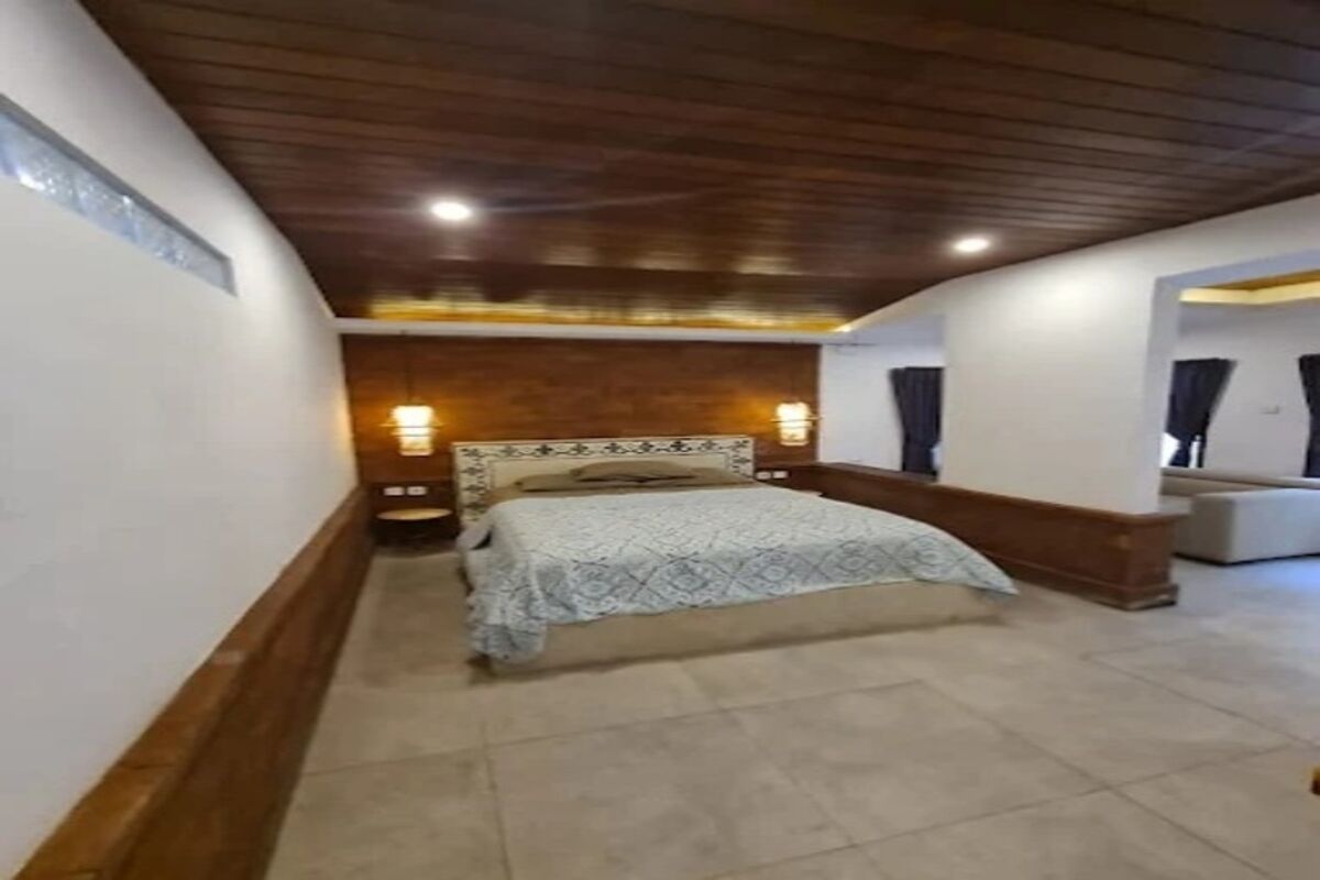 A bedroom with a bed, bedside lamps, a sofa, and a wooden ceiling.