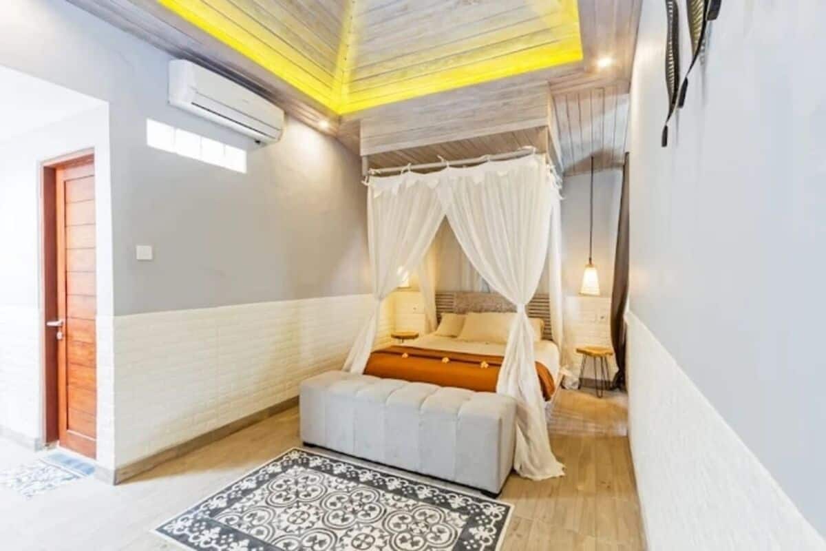 A bedroom with a canopy bed, a bedside table, a lamp, and a small stool.