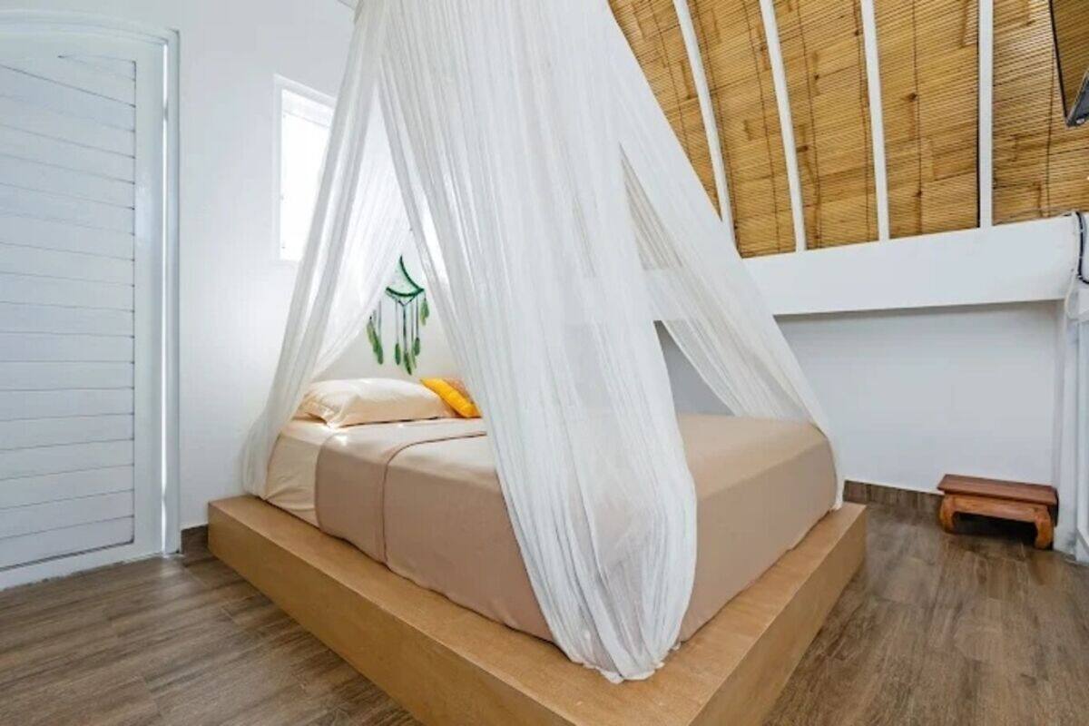 A bedroom with a bed, a small wooden stool, and a window.