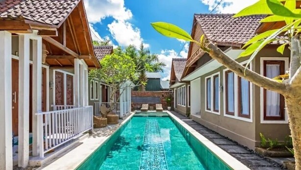 Piscina com cobertura em azulejos, cercada por edifícios com grades brancas e céu claro.