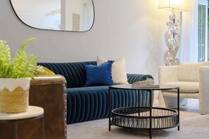 A modern living room with a dark blue sofa, a round coffee table, and a beige armchair.