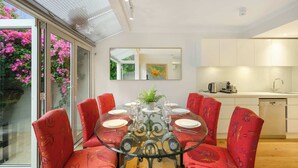 A dining area with a round glass table, red floral chairs, a kitchen with white cabinets, and a large window with pink flowers. - Bright Townhome with Courtyard in Neutral Bay (Neutral Bay)