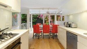 A modern kitchen with a dining area, wooden flooring, and a view of a garden through glass doors. - Bright Townhome with Courtyard in Neutral Bay (Neutral Bay)