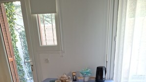 Uma área de refeições com mesa posta para dois, cadeiras, cafeteira e janela com cortinas.