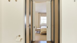 A hallway leading to a bedroom with a bed, a window with curtains, and a toilet paper holder. - The Arch & Lightwell - Chelsea (London)