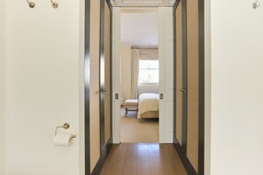 A hallway leading to a bedroom with a bed, a window with curtains, and a toilet paper holder. - The Arch & Lightwell - Chelsea (London)