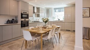 A modern kitchen with white cabinets, a dining table set with placemats, and a vase of flowers. - The Arch & Lightwell - Chelsea (London)