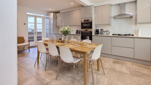 A modern kitchen with a dining area, featuring a wooden table, white chairs, and stainless steel appliances. - The Arch & Lightwell - Chelsea (London)