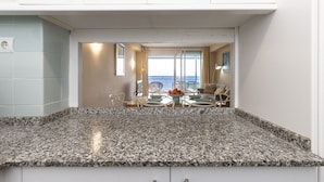 A kitchen with granite countertops, white cabinets, and a view of a dining area with a table and chairs. - Beachfront | Spectacular sea views (La Pineda)