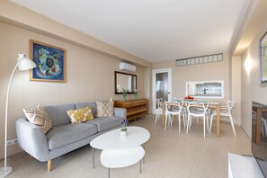 Ein Wohnzimmer mit grauem Sofa, weißem Couchtisch, Esstisch mit Stühlen und einem Bild an der Wand.