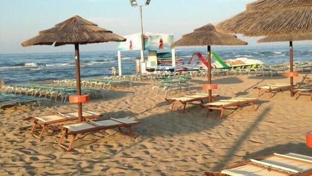 A beach with thatched umbrellas, lounge chairs, and a lifeguard tower. - Hotel Santiago (Rimini)
