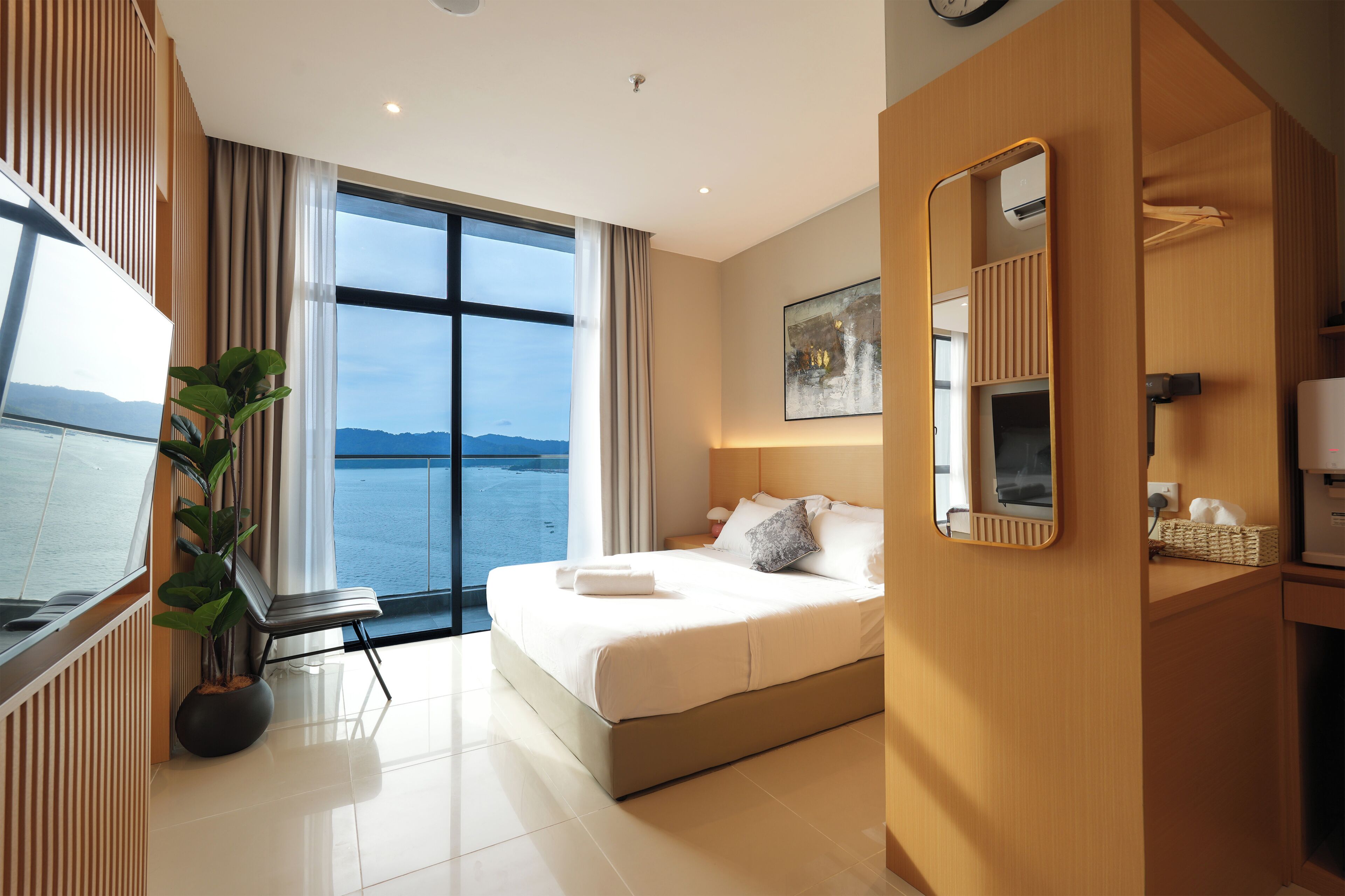 Habitación de hotel moderna con un ventanal grande, una cama, una planta en maceta, un espejo y vistas al mar.