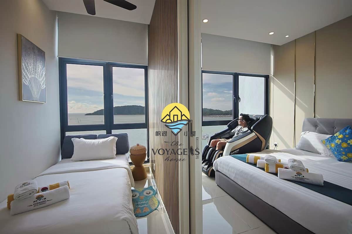 A hotel room with two beds, a massage chair, and a large window offering a view of the sea.