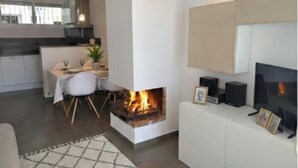 Ein modernes Wohnzimmer mit Kamin, Essbereich und einer Küche im Hintergrund.