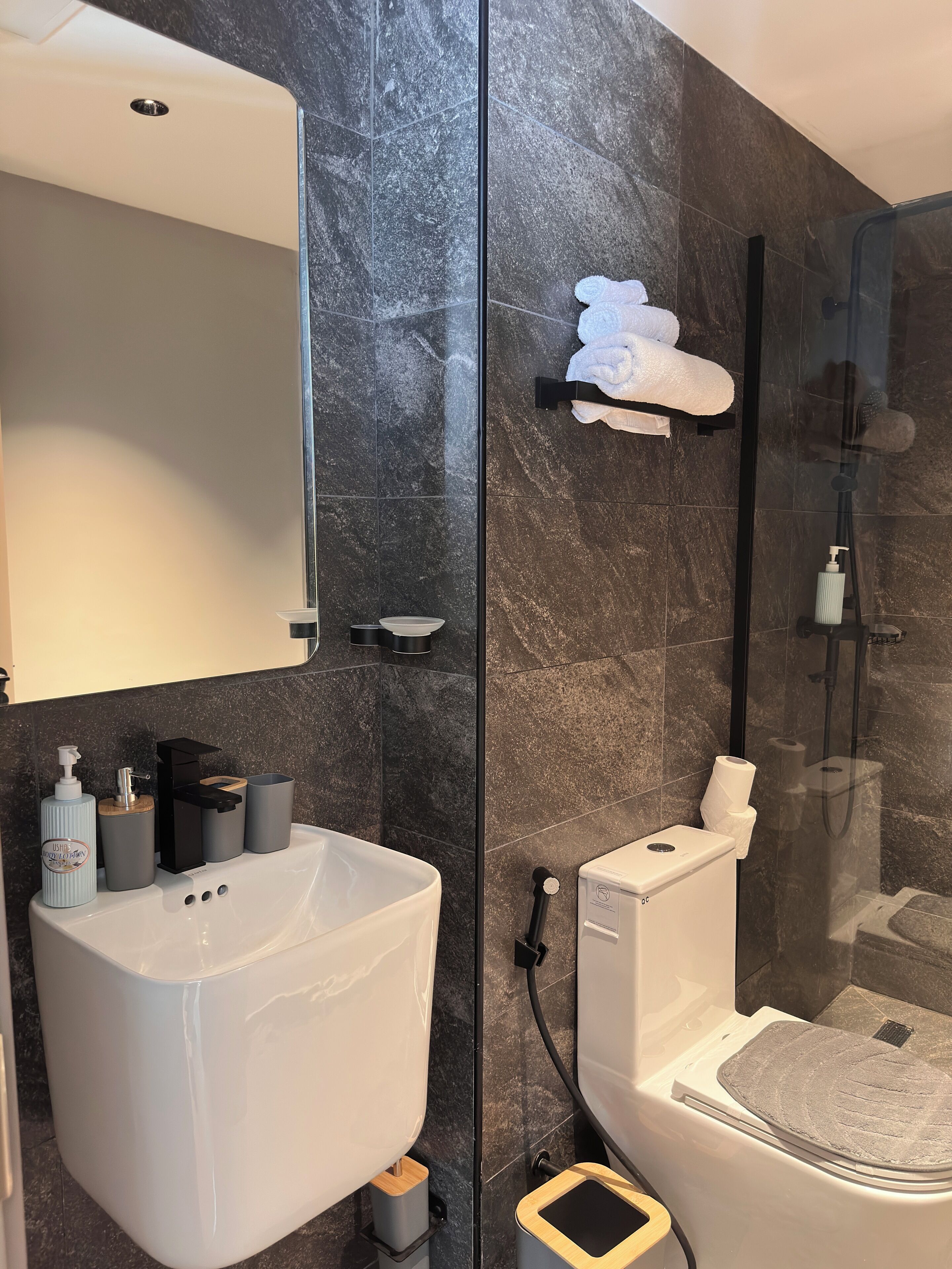 Un baño moderno con un lavamanos grande de color blanco, ducha con cerramiento de vidrio y un perchero para toallas.