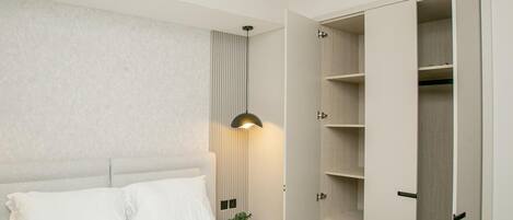 A bedroom with a bed, bedside table, lamp, and open wardrobe.