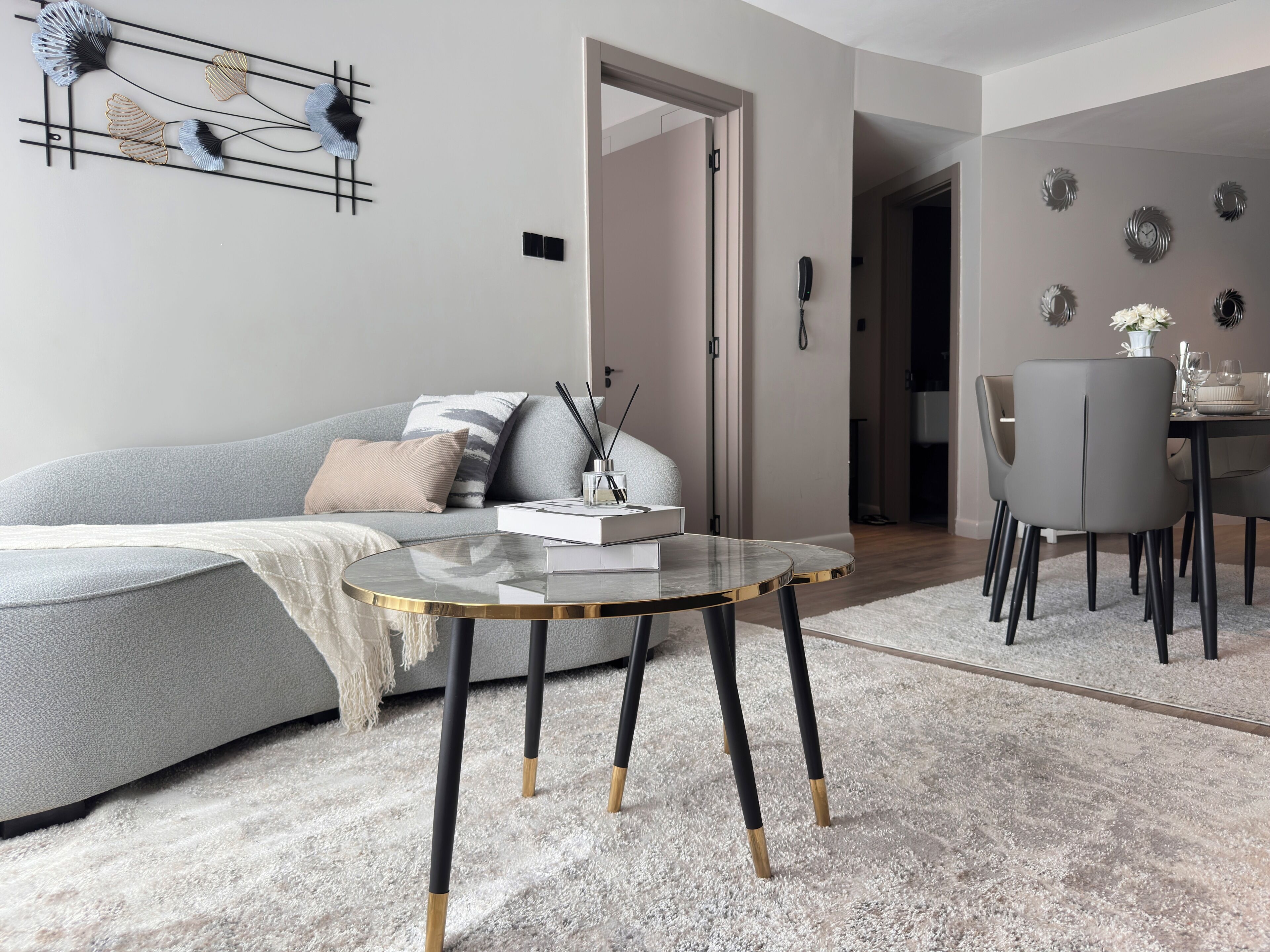A modern living room with a grey sofa, a glass coffee table, and a dining area with grey chairs.
