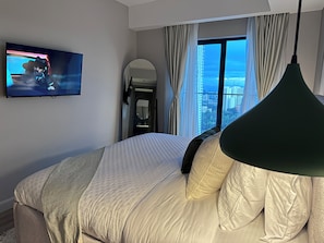 A hotel room with a bed, a TV, a large window with curtains, and a hanging light fixture. - Altura Ruftahomes  (Nairobi)