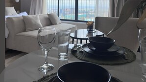 Habitación de hotel con balcón, una mesa de comedor con platos, vasos y un bol, y un sofá con cojines.