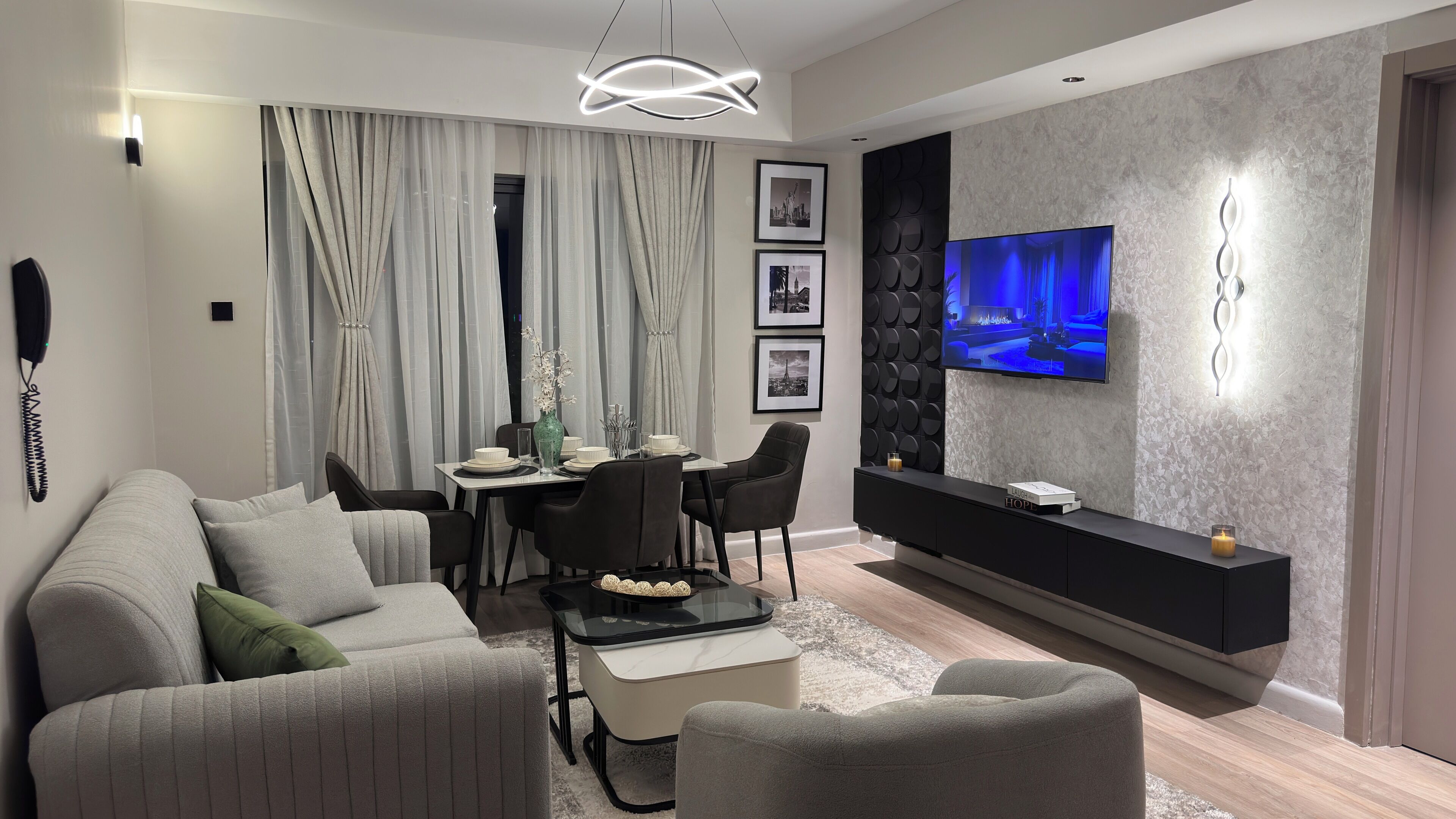 Una sala de estar moderna con un sofá, una mesa de comedor, sillas, un televisor y un mueble de entretenimiento negro.