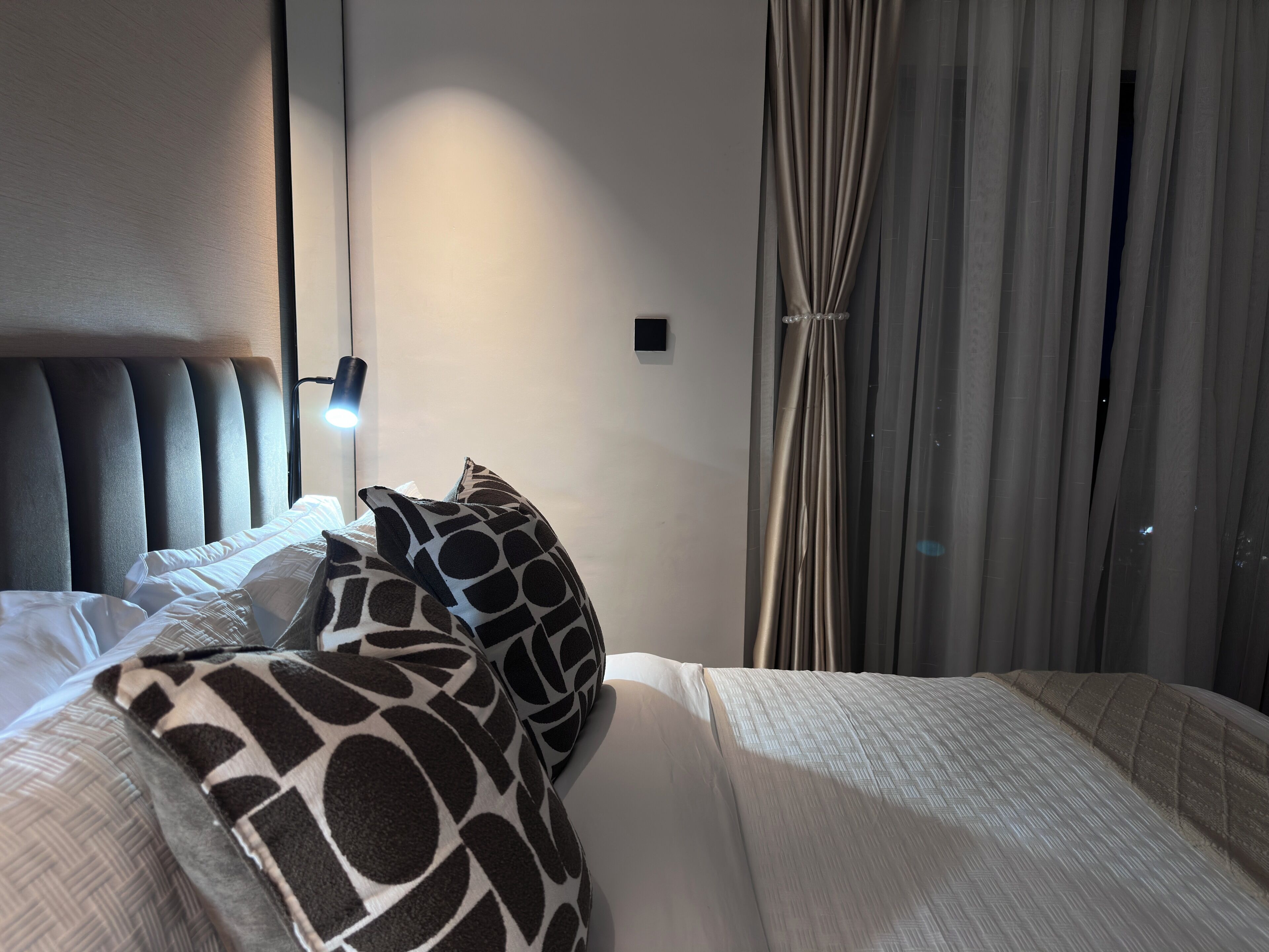 A hotel room with a bed, a headboard, a bedside lamp, a nightstand, and a window with curtains.