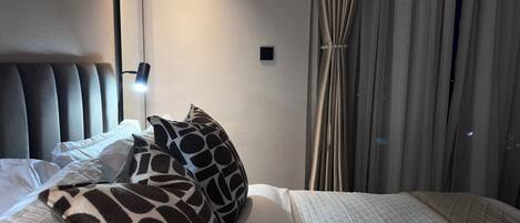 A hotel room with a bed, a headboard, a bedside lamp, a nightstand, and a window with curtains.