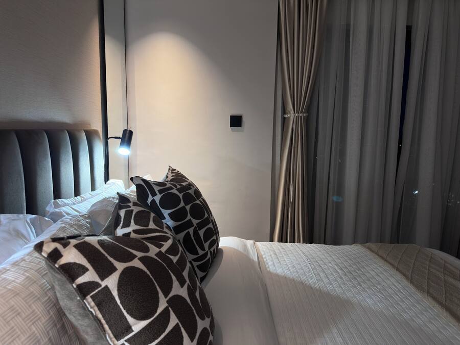 Une chambre d’hôtel avec un lit, une tête de lit, une lampe de chevet, une table de chevet et une fenêtre avec des rideaux.