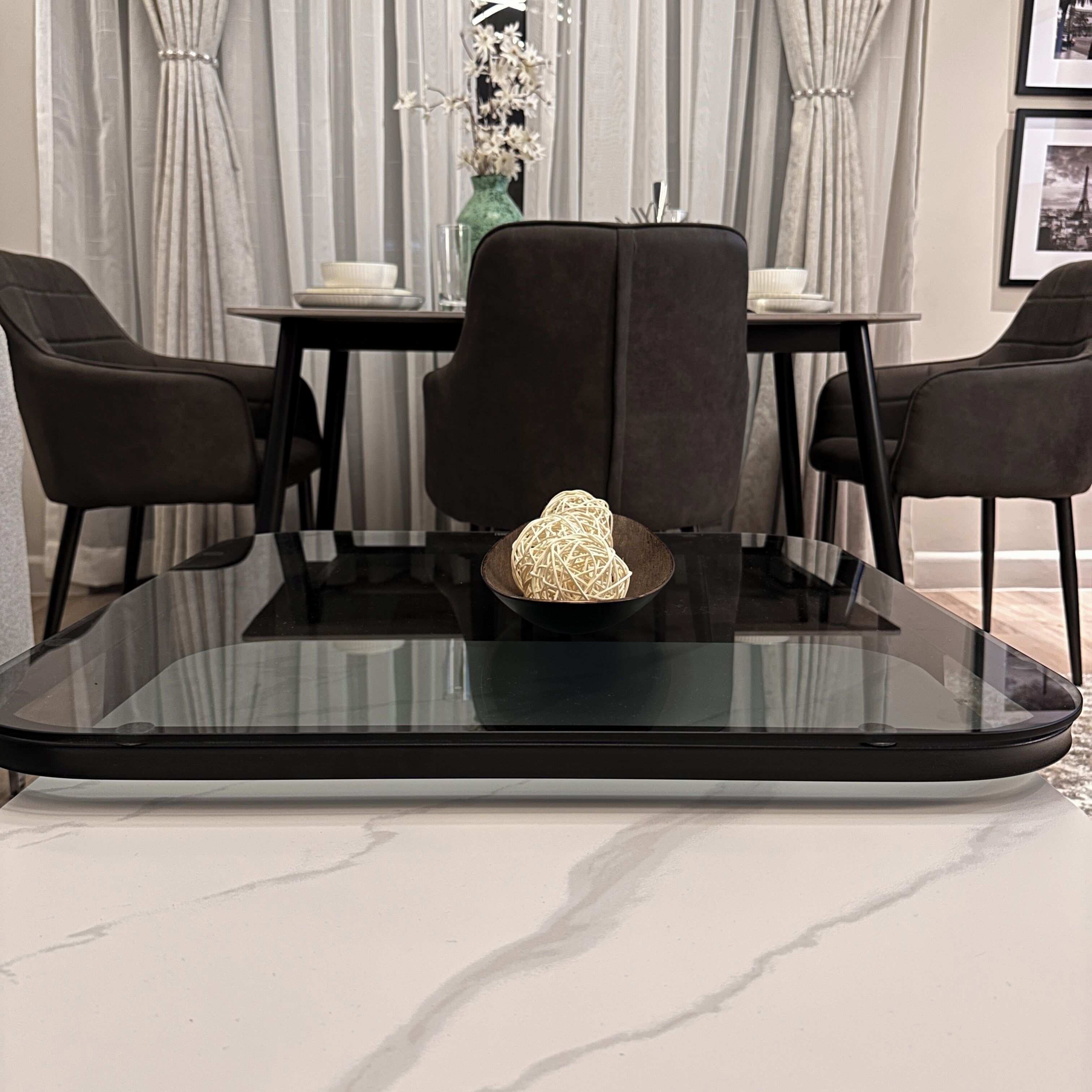 A dining table with a glass top, surrounded by four chairs.