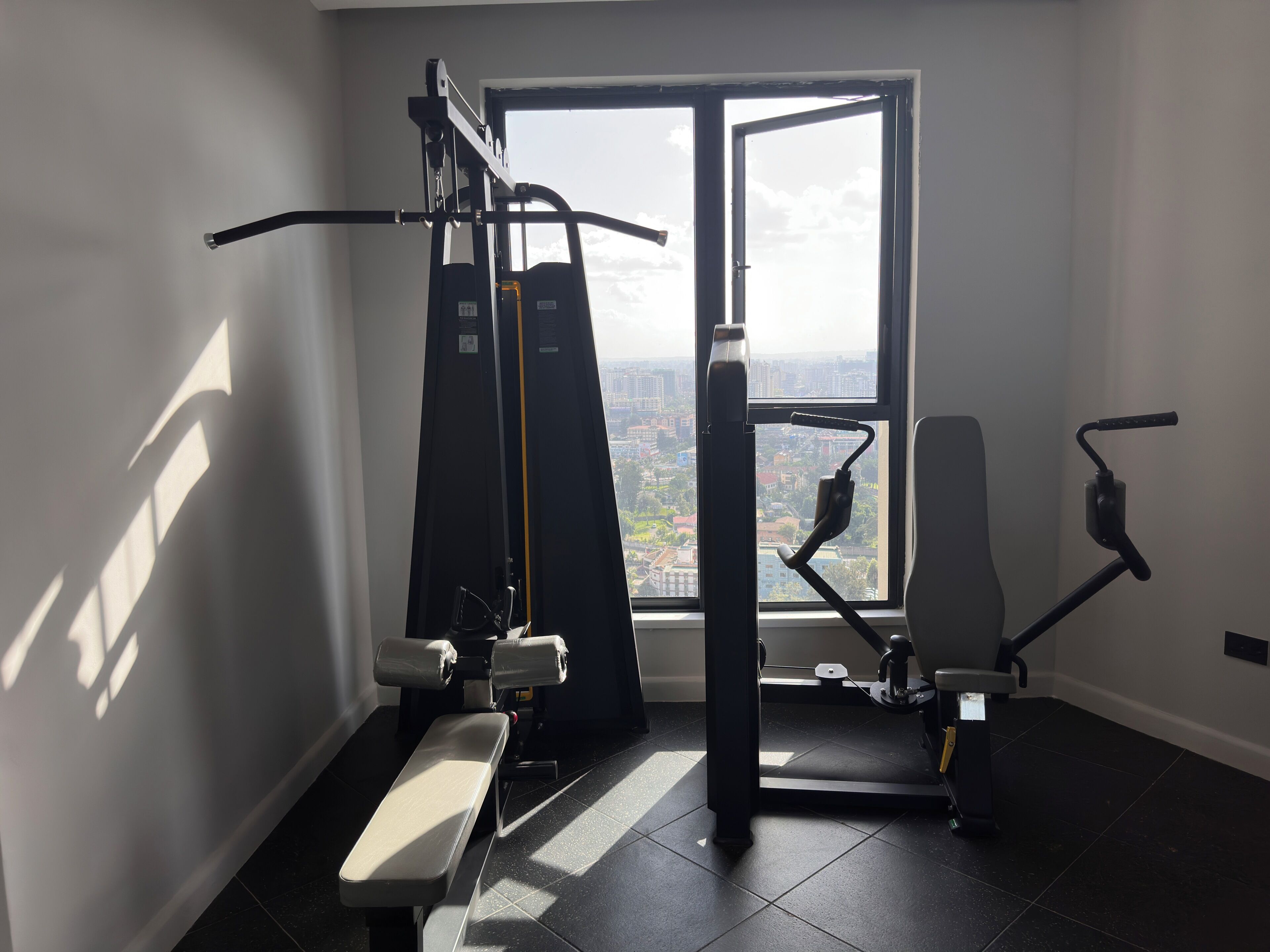 A gym with exercise equipment, a bench, and a window with a city view.