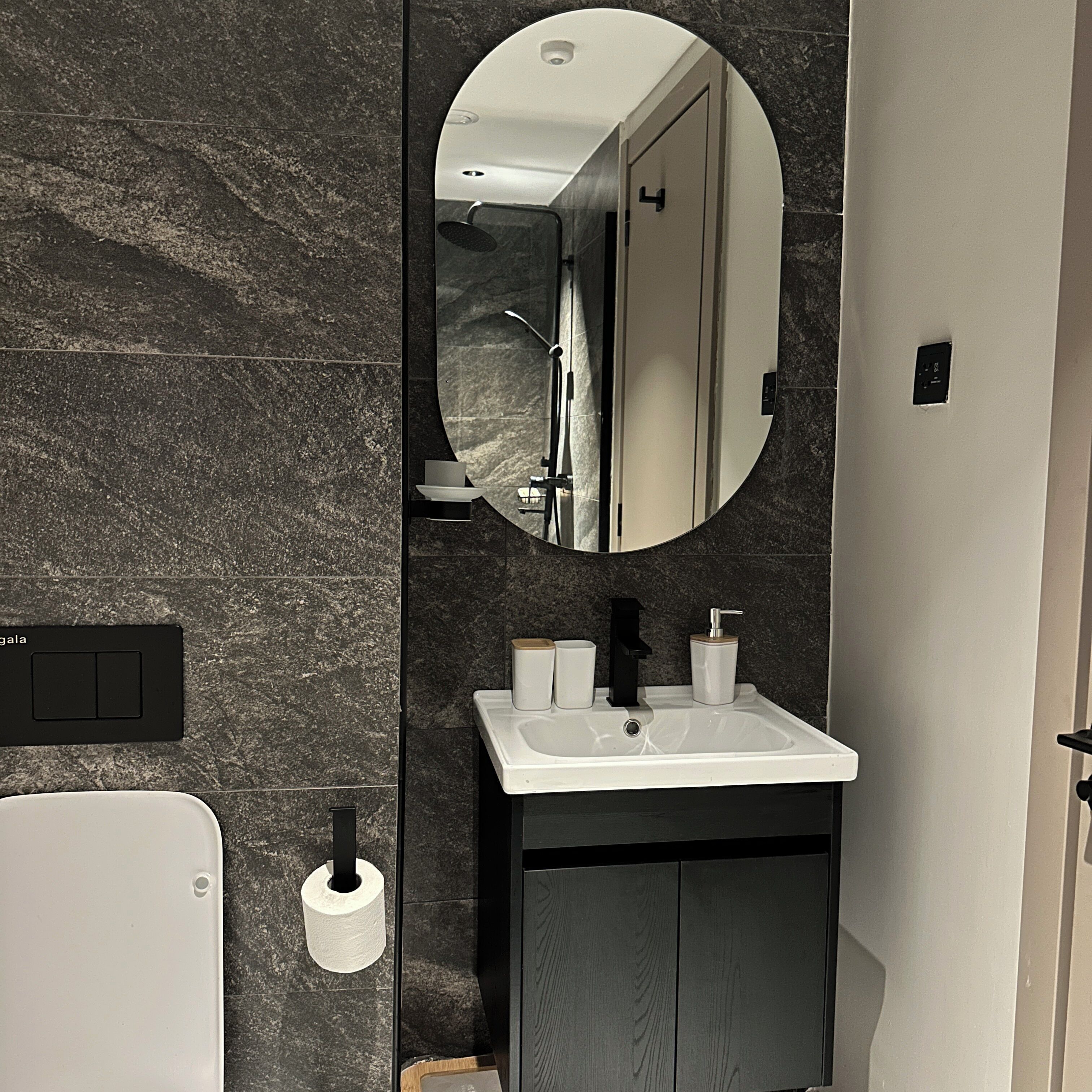 A modern bathroom with a marble wall, a white sink, a mirror, and a toilet.