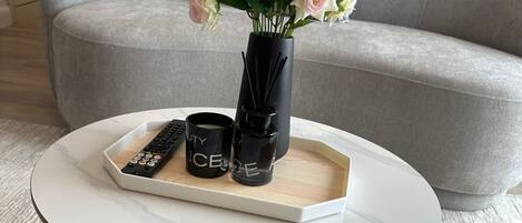 A round coffee table with a tray holding a remote control, two black candles, and a vase of pink roses.