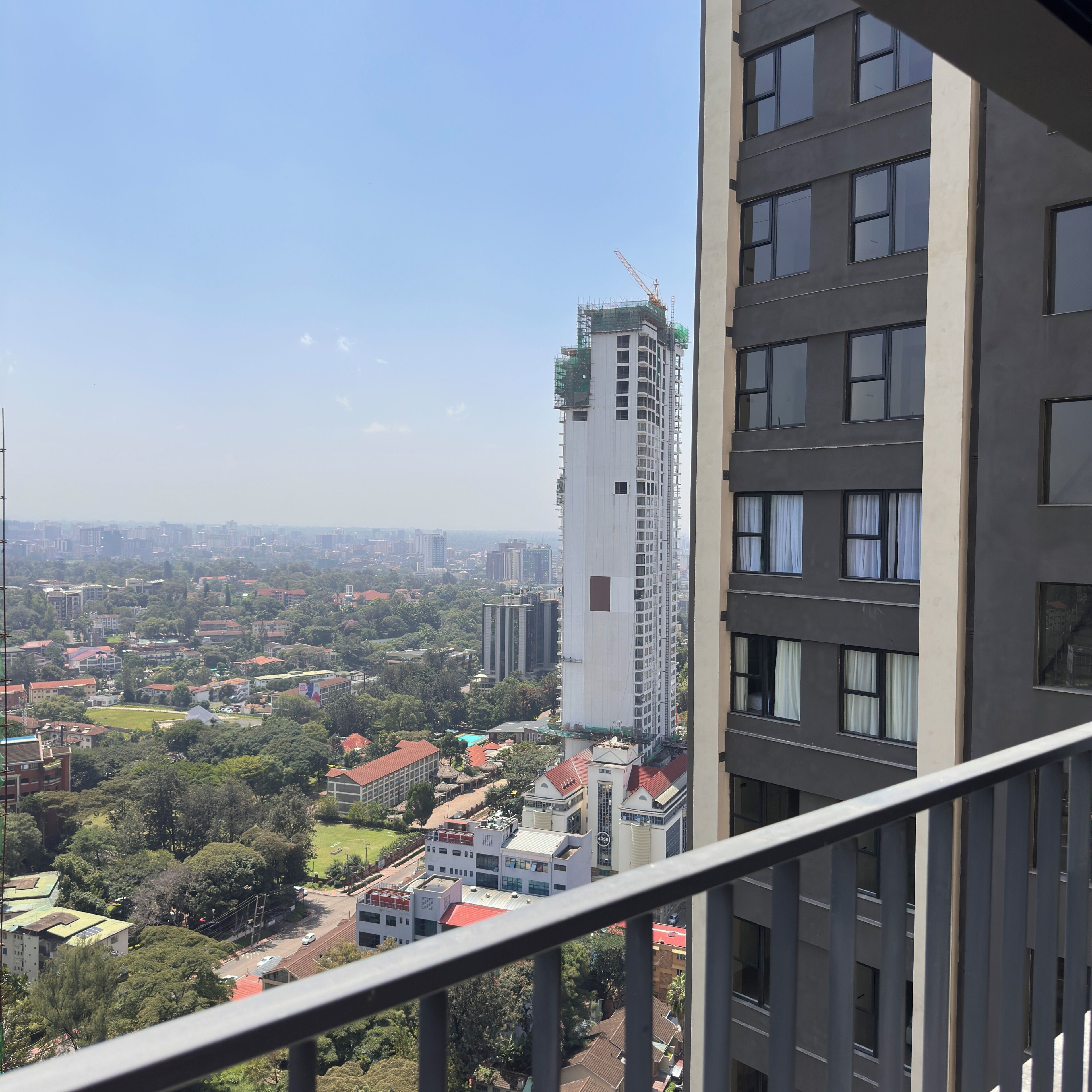 A high-rise building with a construction crane, surrounded by other buildings and greenery.