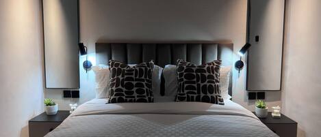 Un dormitorio moderno con una cama grande, dos mesitas de noche, un cabecero y dos lámparas de pared.