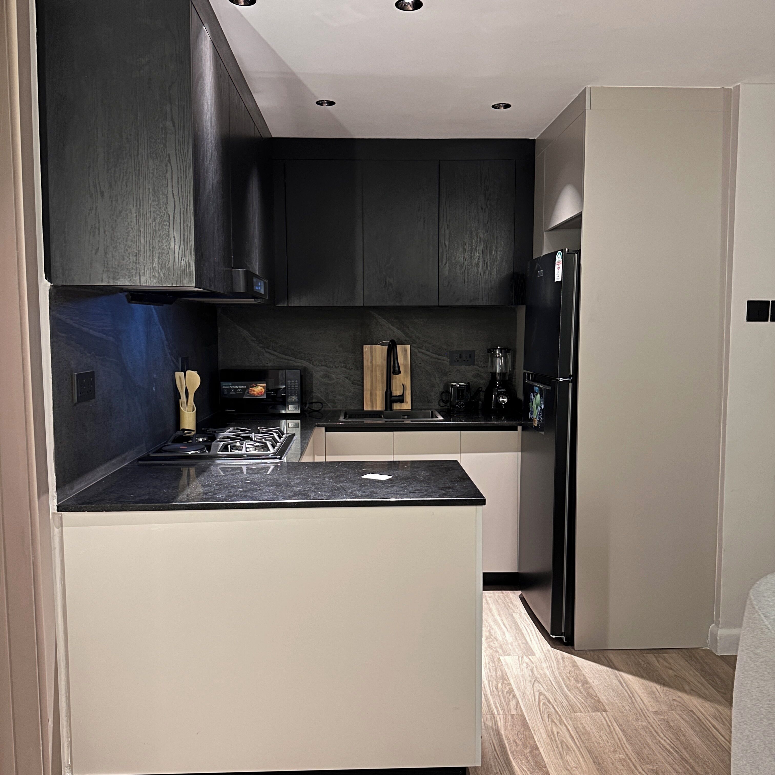 A modern kitchen with dark cabinetry, a black countertop, and a built-in stove.