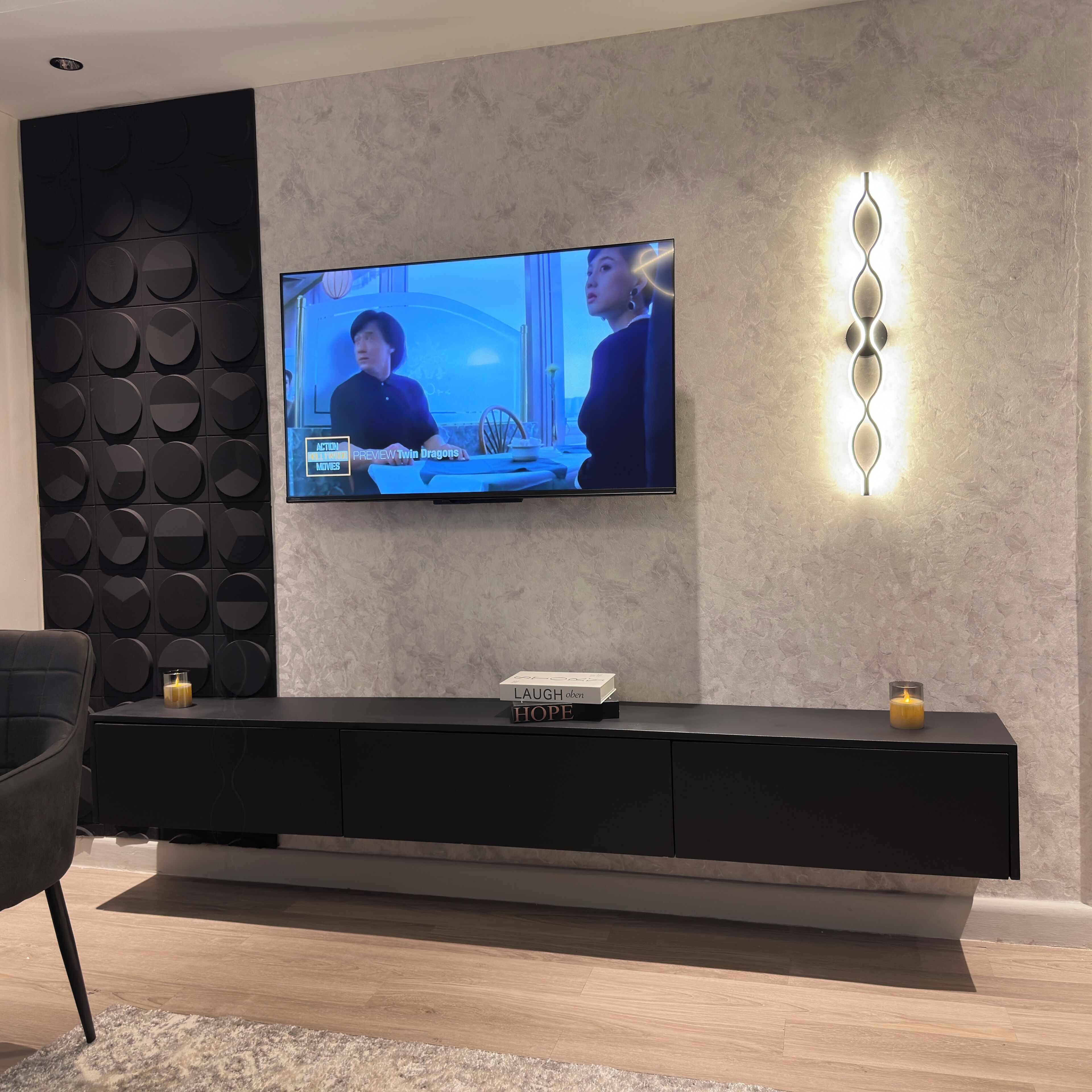 A modern living room with a flat-screen TV mounted on the wall, a black entertainment unit below, and a decorative wall light.