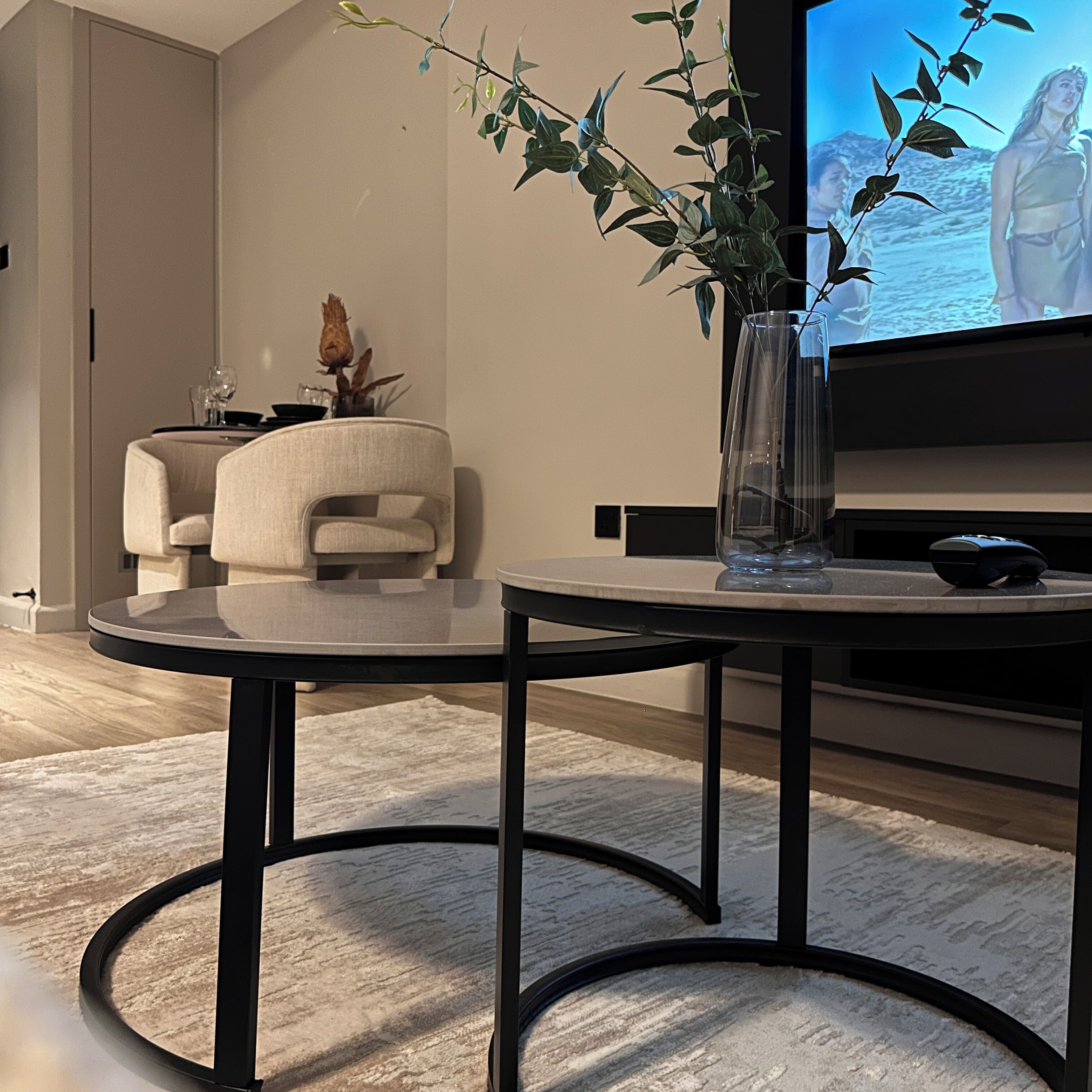 A modern living room with a round coffee table, a sofa, a TV on a stand, and a plant in a vase.