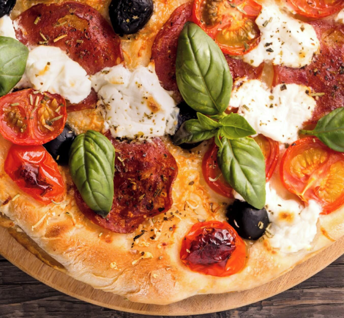 Pizza con ingredientes como tomates, albahaca y queso, sobre una tabla de madera.