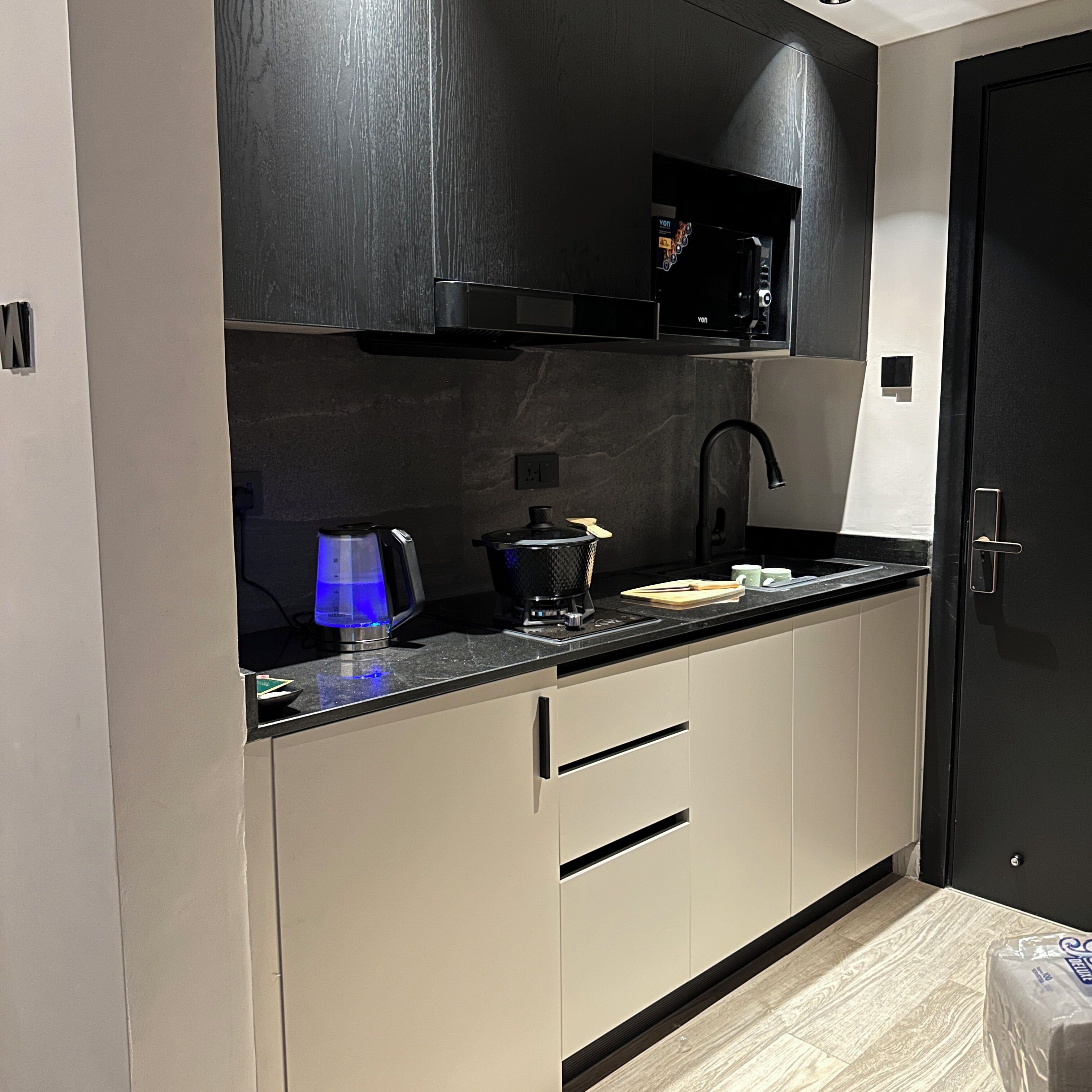 A modern kitchen with a black microwave, a coffee maker, and a blue light.