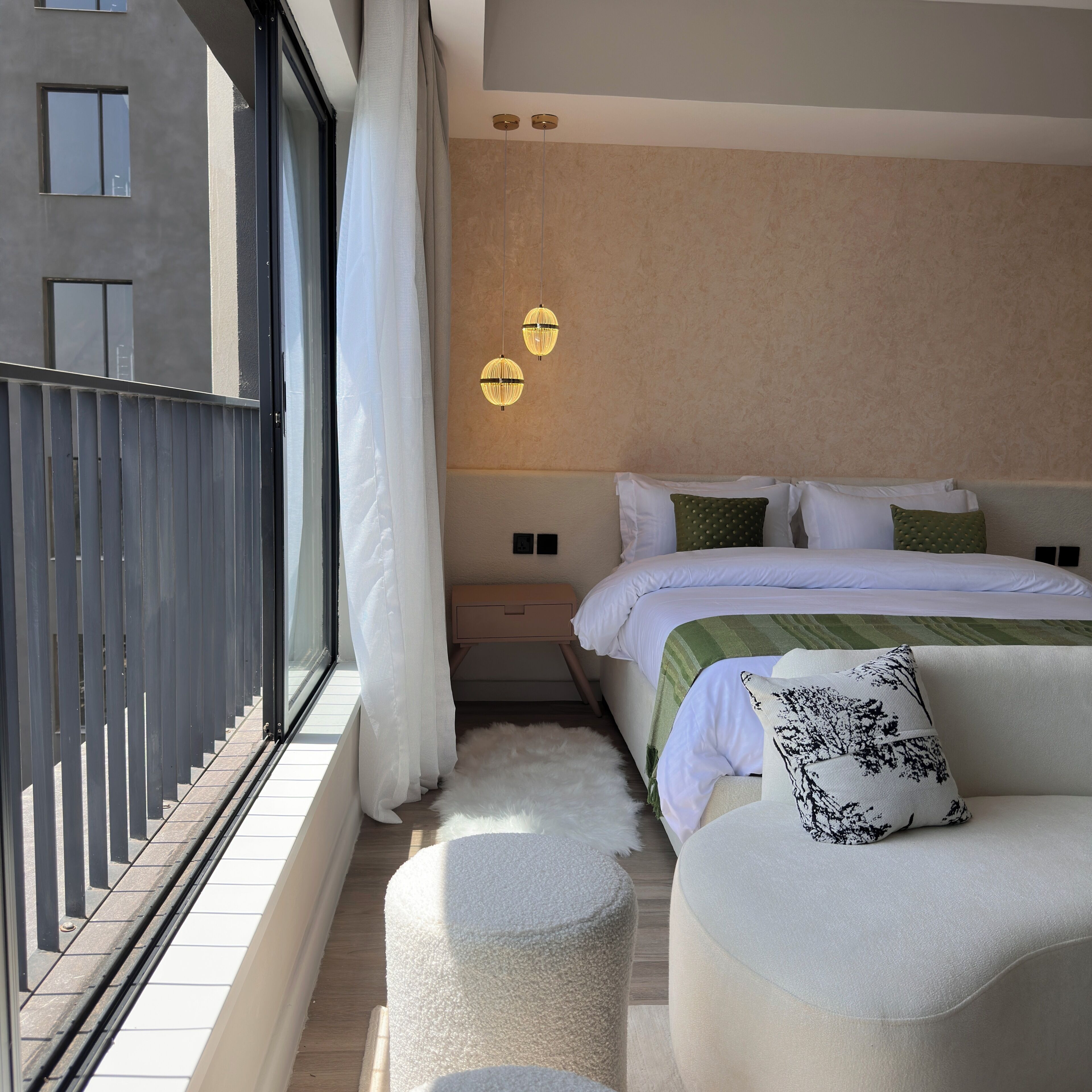 A modern bedroom with a large bed, a nightstand, a sofa, and a view of the outside.