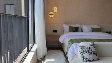 A modern bedroom with a large bed, a nightstand, a sofa, and a view of the outside.