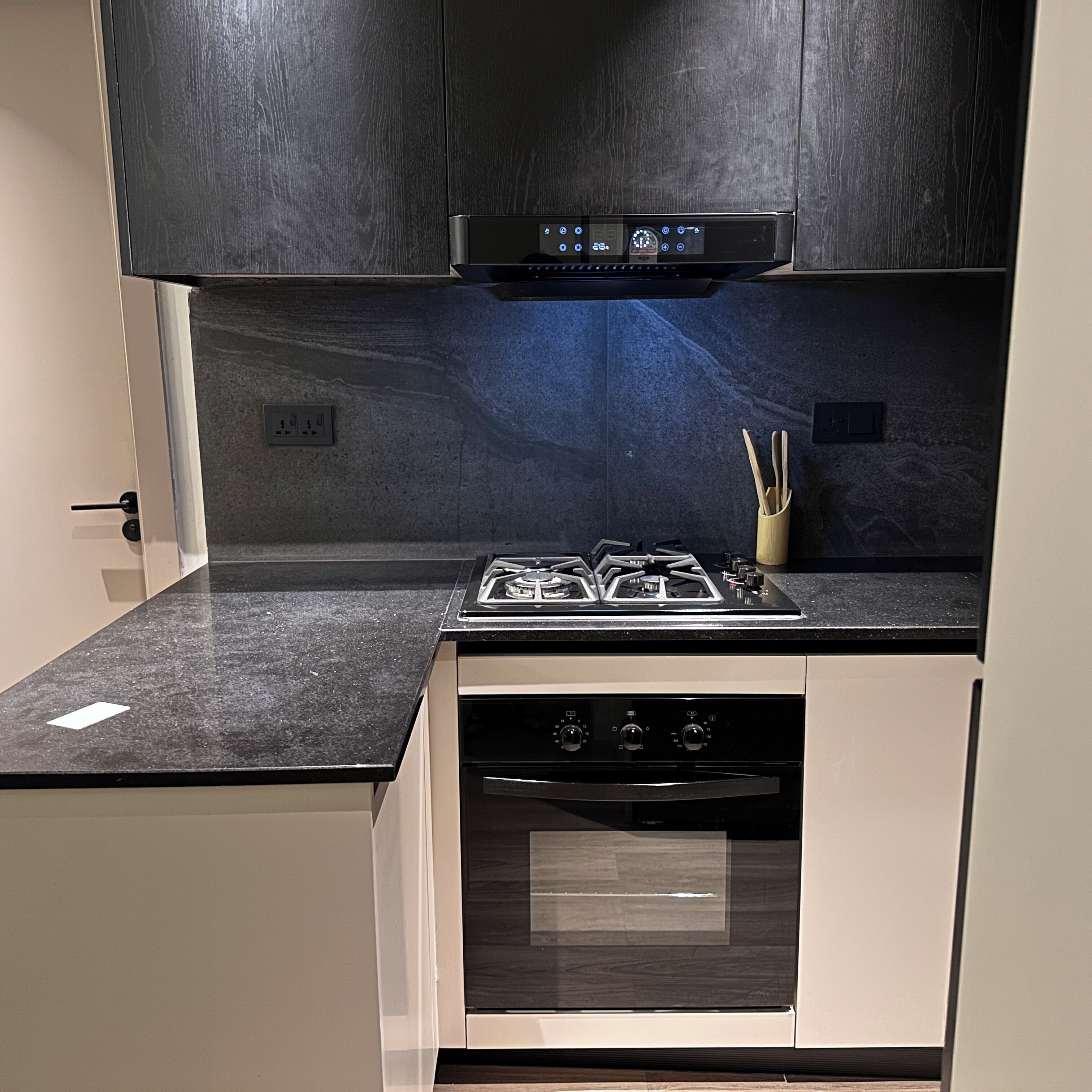 Una cocina compacta con estufa a gas, horno y un salpicadero negro.