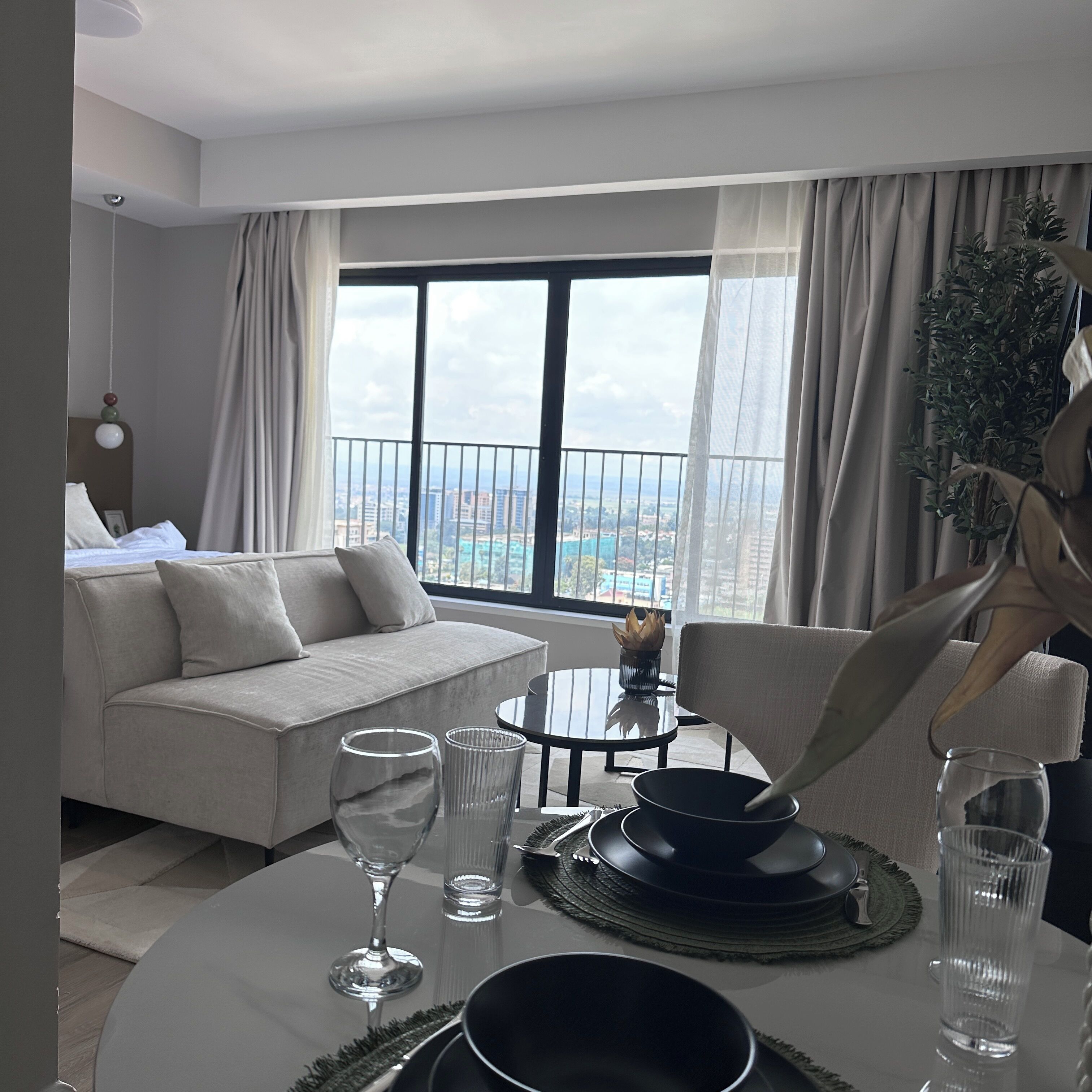 Una habitación de hotel moderna con balcón, un sofá, una mesa de comedor con cubiertos y vistas a la ciudad.