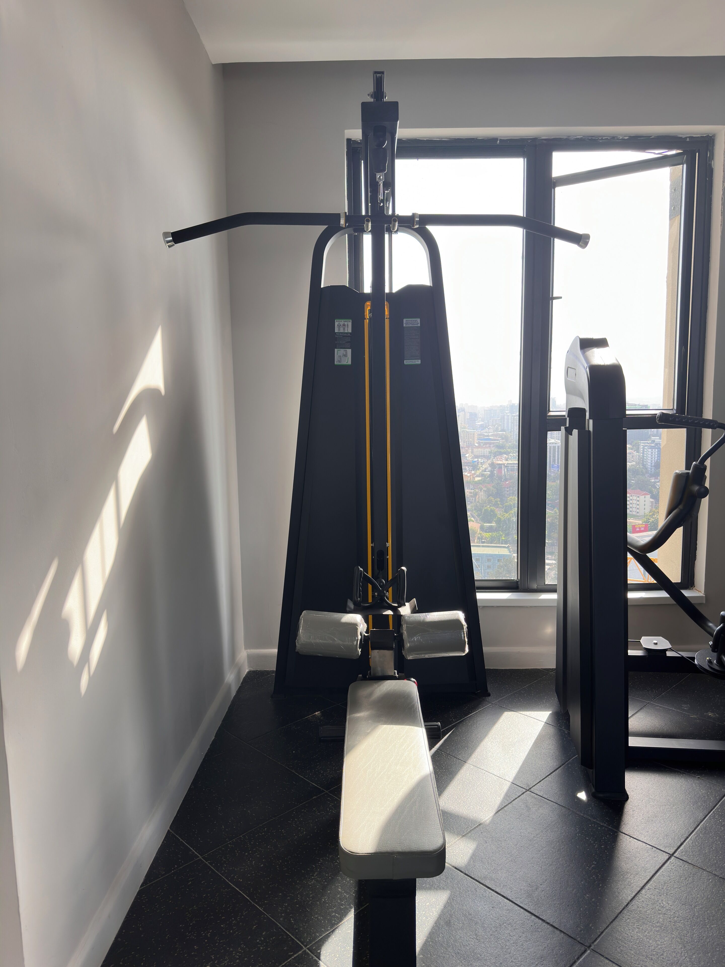 Un gimnasio con equipo de ejercicio, una banca y un ventanal con vistas a la ciudad.