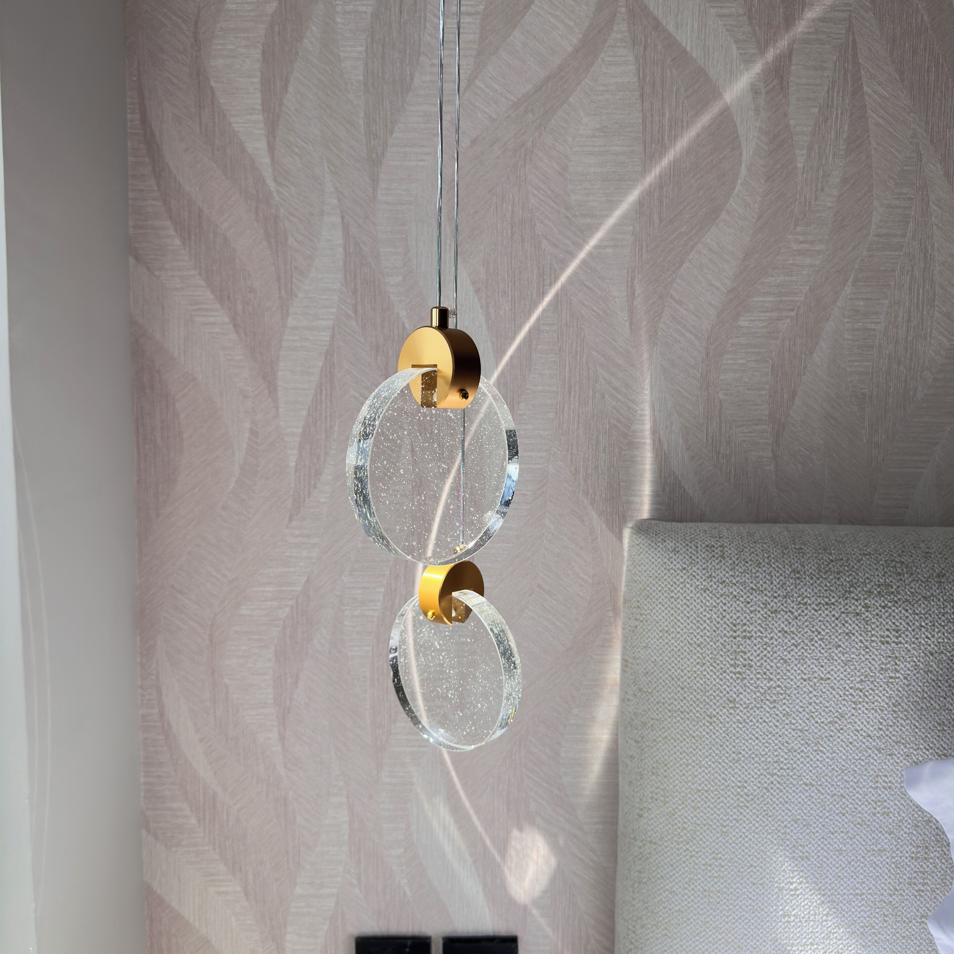 A wall with a herringbone pattern and a hanging light fixture with two circular glass elements and a gold-colored base.