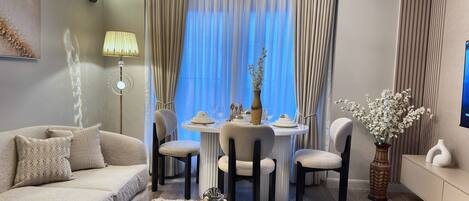 A modern living room with a sofa, a dining table set for two, and a TV mounted on the wall.