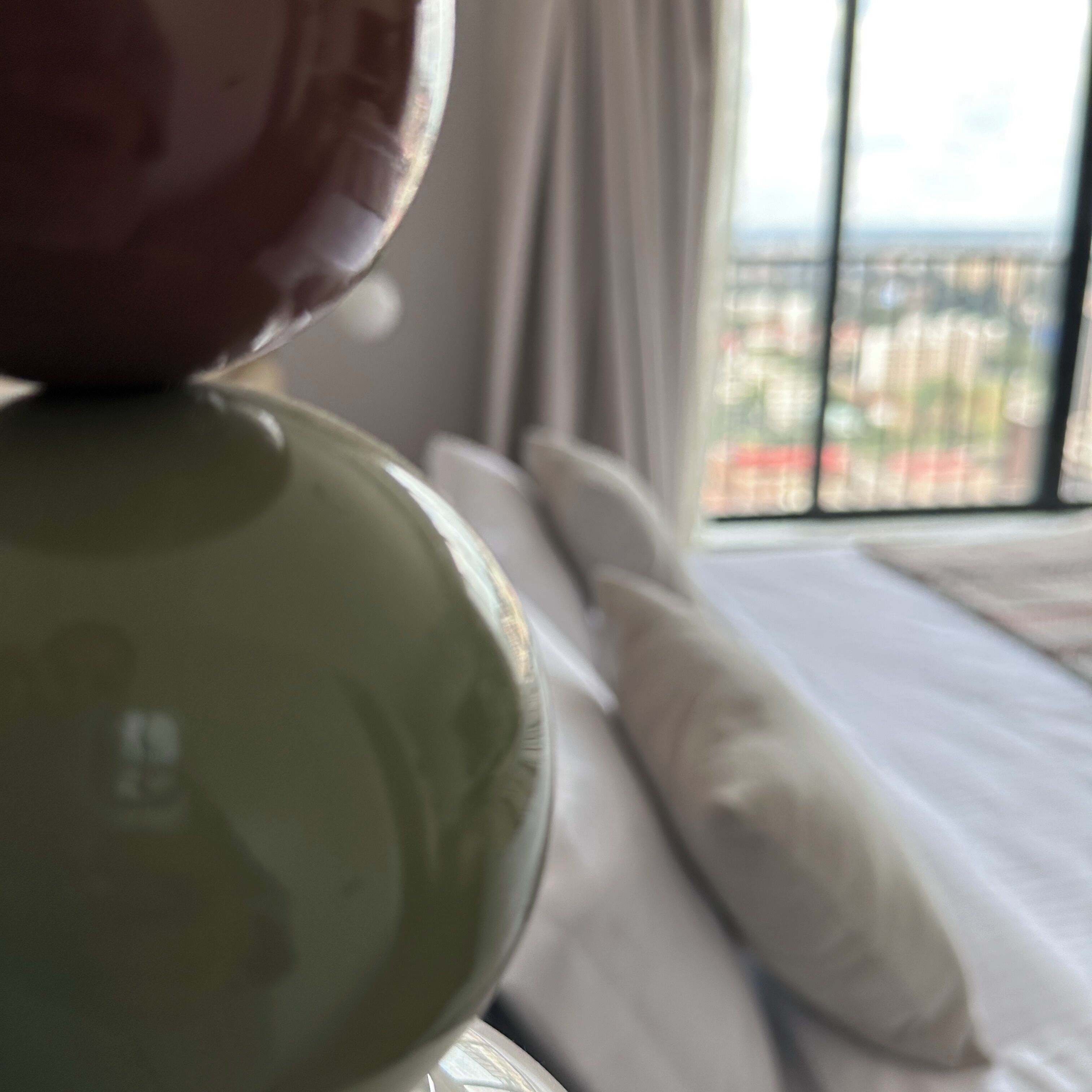 Una cama con un almohadón blanco y vista a una ciudad a través de una ventana.